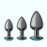The Cheeky Charms Metal Butt Plug Gunmetal Anal Trainer Kit - Teal by Cheeky Charms consists of three black, metallic, teardrop-shaped pieces in small, medium, and large sizes. Each plug is elegantly designed with a teal gem detail at the base and is showcased against a light blue background.